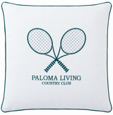 A square white throw pillow with a dark teal border and a central embroidered design of two crossed tennis rackets above the text 'PALOMA LIVING COUNTRY CLUB'.