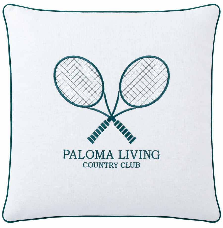 A square white throw pillow with a dark teal border and a central embroidered design of two crossed tennis rackets above the text 'PALOMA LIVING COUNTRY CLUB'.
