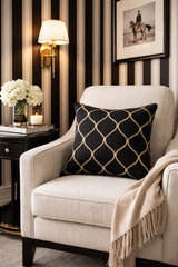 Decorative armchair with a black patterned pillow and beige blanket in a room with striped wallpaper.