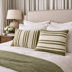 Neatly made bed with striped pillows and a green throw blanket in a bedroom setting.