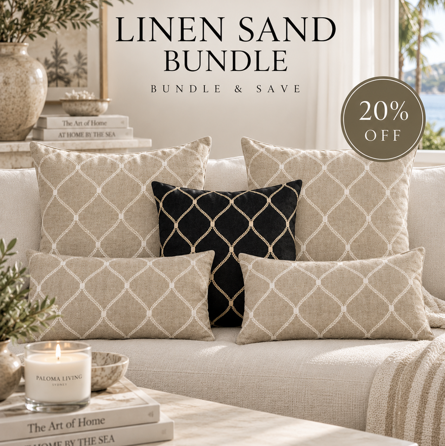 A styled living room scene showing a sofa with multiple throw pillows, including the sold product set. The pillows are in a warm linen sand color with a cream trellis pattern, with one black accent pillow featuring a cream lattice design.